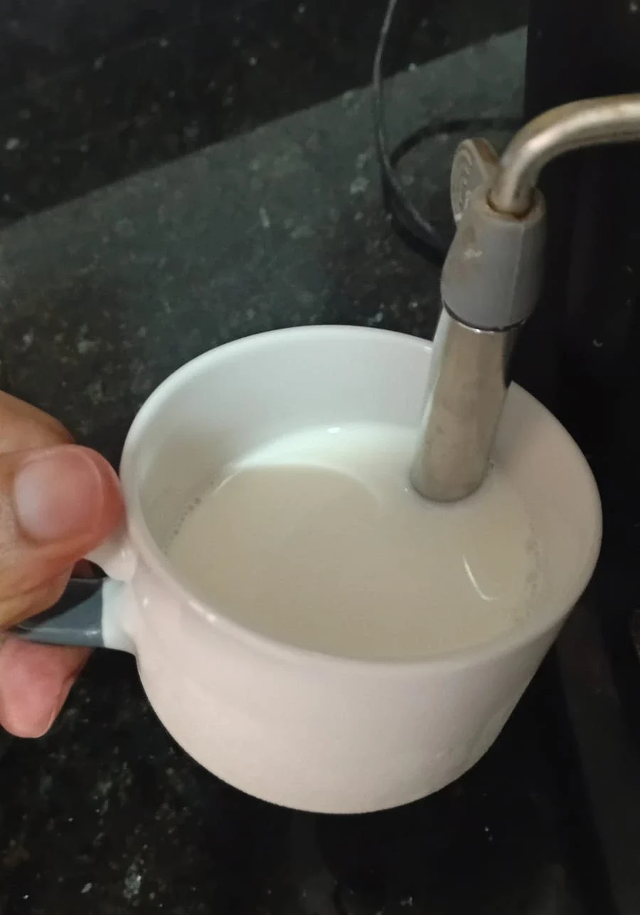 taza de leche debajo de un cilindro de espumador