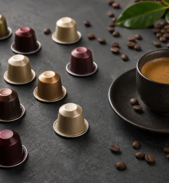 Capsulas de cafe de colores esparcidas alrededor de una taza de espresso sobre fondo oscuro