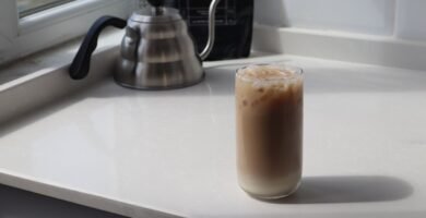 Vaso de cafe helado visto desde arriba junto a una jarra metalica