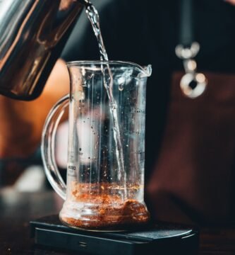 Manos vertiendo agua caliente en una cafetera de vidrio