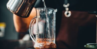 Manos vertiendo agua caliente en una cafetera de vidrio