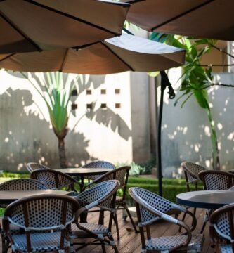 Shaded outdoor cafe terrace with wicker chairs and parasols beside tropical plants