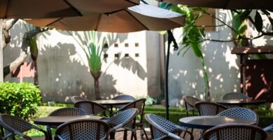 Shaded outdoor cafe terrace with wicker chairs and parasols beside tropical plants