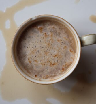 Overhead view of a coffee cup and a fresh coffee spill on a white surface