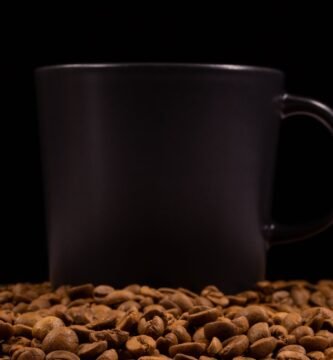 Black mug surrounded by roasted coffee beans on a dark background